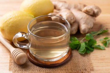 Ahşap zemin üzerinde bardakta limon ve zencefil çayı, sağlıklı sıcak içecek.