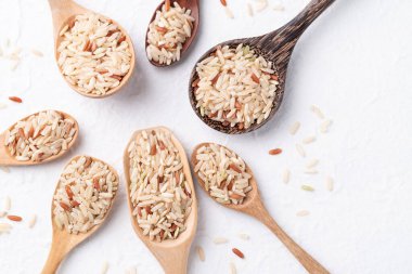 Tayland kahverengi pirinç tohumu (İskoç yabani pirinci) farklı beyaz arka planda ahşap kaşık, üst görünüm