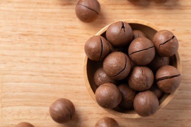 Unpeeled Macadamia nuts in bowl on wooden background, Table top view