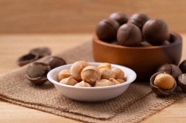 Peeled and unpelled macadamia nuts in a bowl on brown background