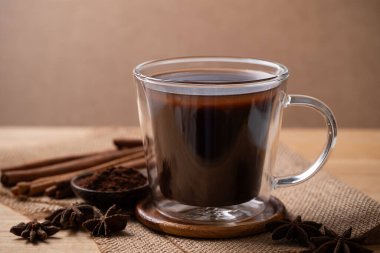 Hot cocoa drink in cup glass with cocoa powder, cinnamon and star anise on brown background