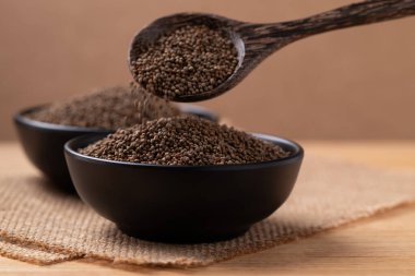 Kahverengi arka planda bir kaseye dökülen kaşık içinde kurutulmuş perilla tohumu.