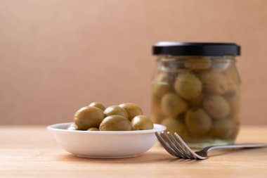 Turşulu zeytin, kapta yeşil zeytin ve tahta zemin üzerinde cam kavanoz.