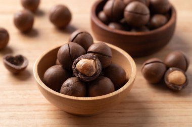 Ahşap arka plandaki tahta kasede Macadamia fındıkları.