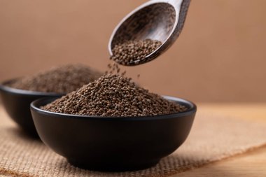 Kahverengi arka planda bir kaseye dökülen kaşık içinde kurutulmuş perilla tohumu.