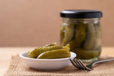 Salatalık turşusu ya da Gherkin turşusu kahverengi arka planda bir kase ve cam kavanozda.