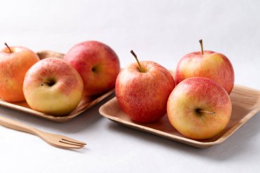 Beyaz zemin üzerinde ahşap çatalla doğal tabakta kırmızı elma (gala elması)