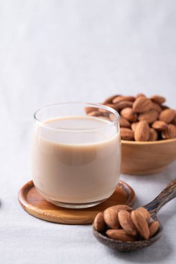 Beyaz kumaş arka planda bir bardak badem sütü ve badem fıstığı, bitkiden yapılmış alternatif süt, sütsüz süt.