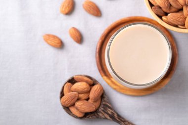 Beyaz kumaş arka planda bir bardak badem sütü ve badem fıstığı, bitkiden yapılmış alternatif süt, sütsüz süt.