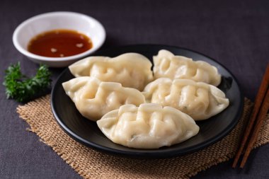 Siyah bir tabakta susam yağı sosuyla servis edilen enfes buğulanmış hamur köftelerini yakından çek.