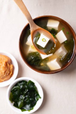 Sağlıklı Japon miso çorbasının üst görüntüsü yumuşak tofu ve ahşap bir kasedeki yosun kaşıkla kepçeleniyor.