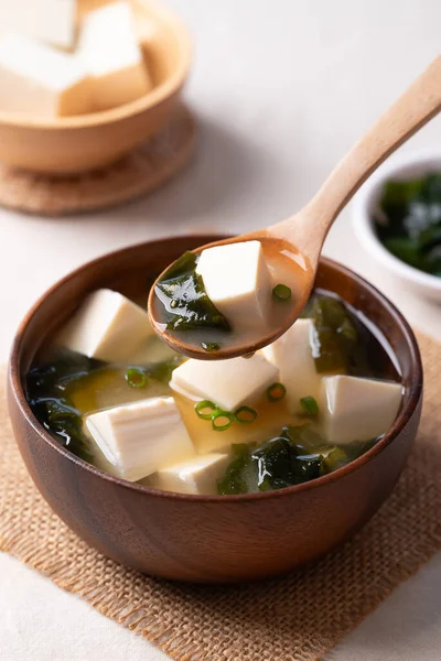 Sağlıklı Japon miso çorbası. Yumuşak tofu ve yosun. Tahta bir kasede kaşık ile kepçeleniyor.