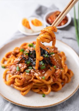 Kızarmış Udon şehriyesini kimchi, lahana, domuz, taze soğan, susam tohumu ve çubuklarla yenen yosunla karıştır.