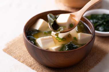 Sağlıklı Japon miso çorbası. Yumuşak tofu ve yosun. Tahta bir kasede kaşık ile kepçeleniyor.