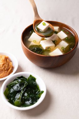 Sağlıklı Japon miso çorbası. Yumuşak tofu ve yosun. Tahta bir kasede kaşık ile kepçeleniyor.