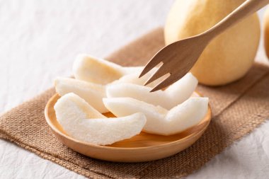 Tahta bir tabakta dilimlenmiş Asya armutları ve yemeye hazır bir çatal.