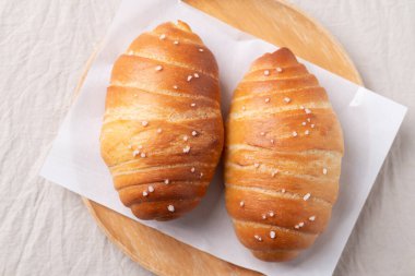 Beyaz kumaş kaplamalı ahşap tabakta deniz tuzu taneleri ve Japon fırın tarzında tuzlu ekmek (Shio pan).