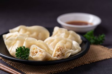 Domuz eti, tavuk ve sebzelerle dolu buharda pişirilmiş hamur köftelerini siyah tabakta, susam yağı sosuyla servis et.