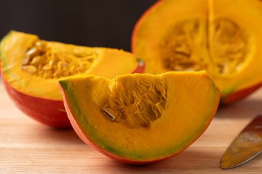 Dilimlenmiş portakallı Kuri kabağı (Hokkaido kabağı) tahta bir kesme tahtasının üzerinde bıçakla yemek pişirmeye hazırlanıyor.