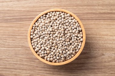 Ahşap zemin üzerinde ahşap bir kasede beyaz biberlerin üst görüntüsü, temel baharatlar ve yemek pişirmek için baharatlar.