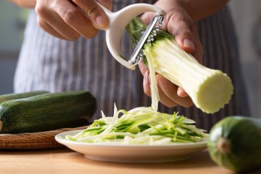 Eller jülyen soyucuyu kullanarak yeşil kabağı erişteye çevirerek sağlıklı yiyecekler hazırlıyor.