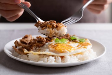 Kızarmış domuz eti, sarımsak, biber, sahanda yumurta ve beyaz bir tabakta pilav, kaşık, çatal ve yemek. Tayland sokak yemeği tarzı.