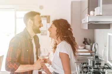 Genç çift mutfakta bir bardak beyaz şarap içiyor. Birbirlerine aşık çiftler yeni evlerinin tadını çıkarıyorlar. Arka planda sıcak bir ışık var.