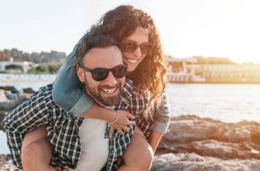 Kucaklaşan ve kumsal tatilinde eğlenen sevgi dolu çift - erkek, bir ilişki konseptinde erkek ve kız arkadaşını sırtında taşır -