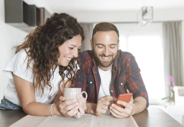 Young couple laughs while using smartphone - couple in love having breakfast together and reading the latest news using mobile phone