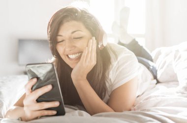 Kulaklıklı akıllı telefon kullanan güzel bir bayan müzik dinlemekten, oyun oynamaktan ve sohbet etmekten keyif alıyor.