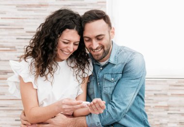 Hamilelik testi sonuçlarını okuyan genç bir çiftin portresi. Evli bir çift, arka planda sıcak bir işaret ateşi görmeyi bekliyor.