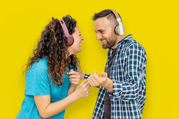 Couple on yellow colored background is having fun and dancing listening to music with headphones