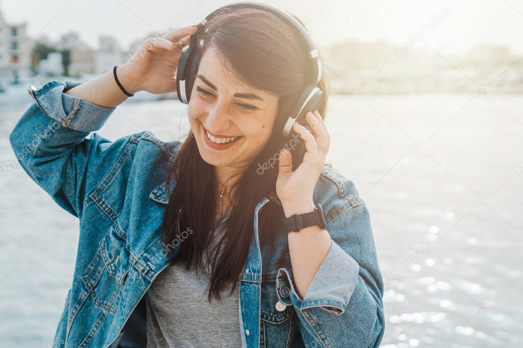 Young woman listens to music and podcasts with portable headphones - flare on background