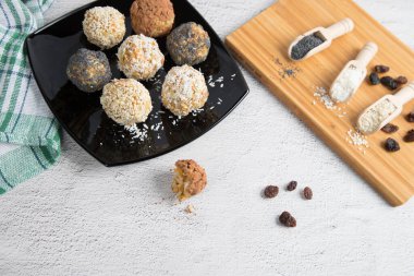 Kurutulmuş meyve, fındık, susam tohumu, kakao, badem ve siyah tabakta haşhaş tohumu, ahşap kesme tahtasındaki ahşap kaşıklardaki baharatlar, kemirilmiş bir top. Vejetaryen ve vejetaryen çiğ aperatif veya yiyecek. Kapat..