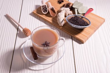 Bir fincan sıcak Hint çayı, baharatlı kaşıklar, zencefil, kesme tahtasında anason, beyaz arka planda. Yatay yönelim.