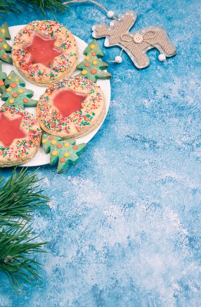 На синем фоне тарелка с рождественским печеньем ручной работы, сосновыми ветвями и рождественским украшением в виде оленя. Вертикальное направление. Копирование пространства — стоковое фото