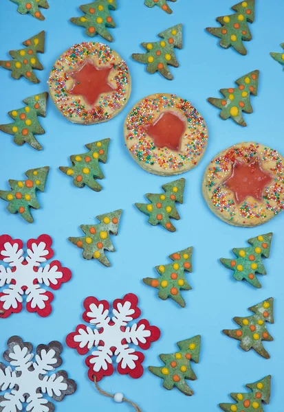 Zelfgemaakte kerstkoekjes Kerstbomen en -ringen met glazuur en kerstversieringen in de vorm van sneeuwvlokken zijn in een patroon op een blauwe achtergrond gelegd. Verticale oriëntatie — Stockfoto