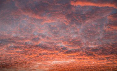 Gökyüzündeki küçük bulutlar gün batımında kırmızıya vurgulanır. Yatay yönelim.
