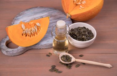 Tahta kesim tahtasında dilimlenmiş bir balkabağı, bir şişe balkabağı yağı ve tahta kaşıkta kabak çekirdeği. .