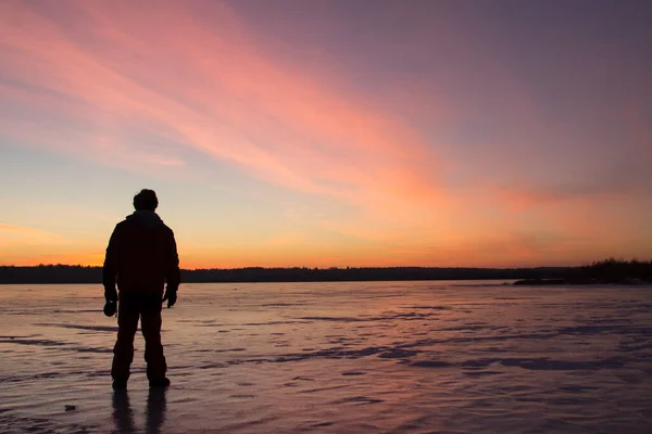 Silhouette of a man at sunset standing on the ice of a frozen lake. Winter background