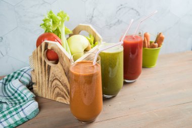 Vitamin sebze suları havuç, kereviz ve domates vitaminleri cam bardaklarda ahşap zemin üzerindedir. Arka planda sebze ve meyve içeren ahşap bir kutu. Sağlıklı Yeme Konsepti