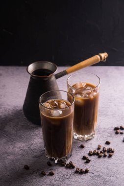 İki büyük bardak sütlü ve buzlu soğuk kahve makinesiyle koyu bir arka plan ve dağınık doğal kahve taneleri. Uzayı kopyala Yaz için ferahlatıcı içecek konsepti