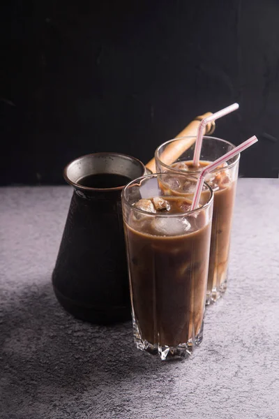 Coffee maker with two tall glasses of cold coffee with milk and ice on a dark background . Copy space. The concept of refreshing drinks for summer