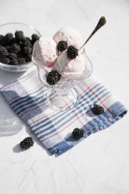 Bir kase dondurma ve böğürtlen mavi kareli peçetenin üzerinde duruyor. Kapat. Dikey yönelim.