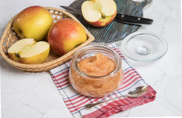 Apple puree in a glass jar and fresh apples on a light background. Close up. Horizontal orientation.