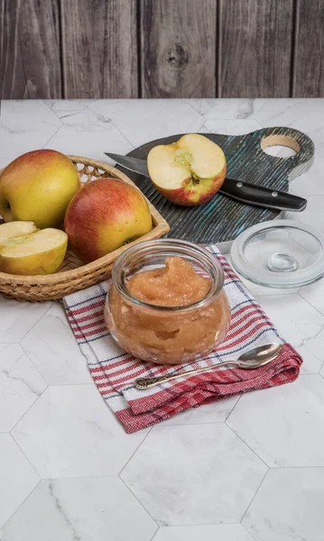 Apple puree in a glass jar and fresh apples in a plate on a light background. A place for a space mine. Horizontal orientation.