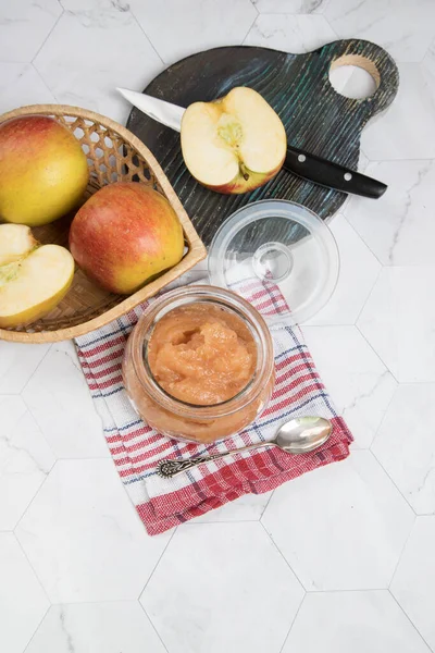 Glass jar with Apple puree and fresh apples in a plate on a light background with a checkered napkin. Flat lay.Vertical orientation.