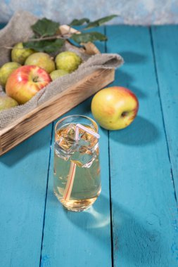 Elma ve armut suyu bardakta, elmalar ve armutlar ahşap tepside peçeteyle, bir Apple yanında, renkli ahşap zemin. Kapat. Dikey yönelim