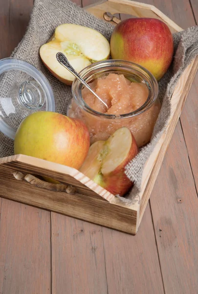 Wooden tray with a jar of Apple puree and fresh apples on a wooden background . Close up. Vertical orientation.