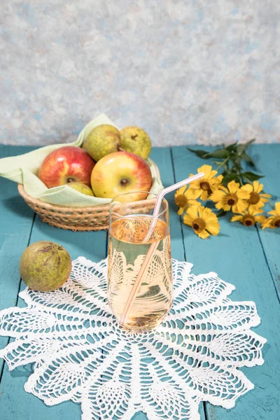 Apple juice in a glass on a lace napkin, juice in a jug, apples on a plate, colored wooden background. Vertical orientation